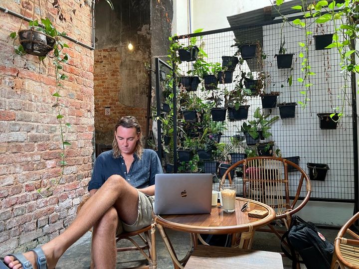 Digital nomad working in a café with a Apple MacBook laptop, hanging plants, coffee, Bean Sprout Café,Georgetown, Penang