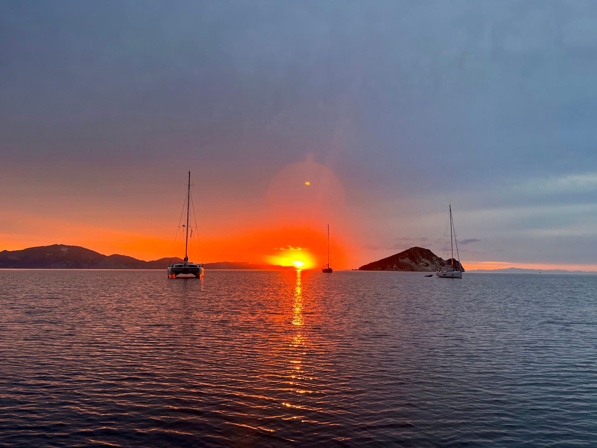 On the ocean looking at the sunrise at Keri, Zakynthos, Greece. One catamaran at the left and two sailboats.